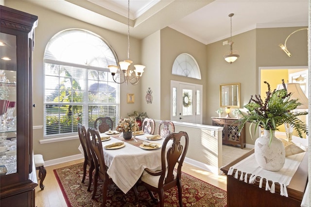 dining space with crown molding, a high ceiling, a chandelier, light wood-type flooring, and baseboards