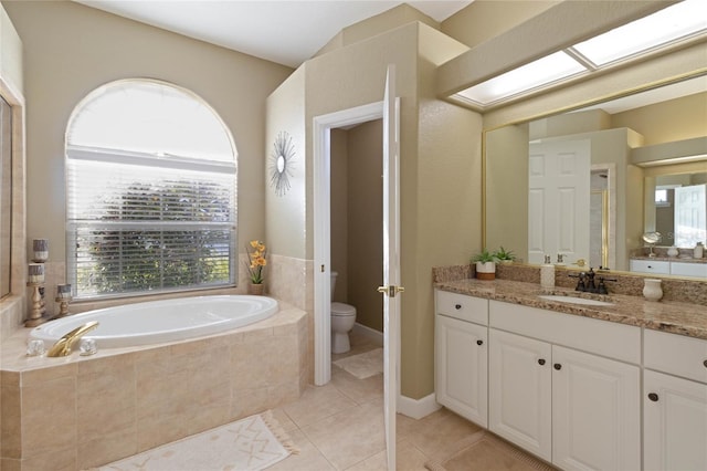 full bath with a skylight, toilet, vanity, a bath, and tile patterned floors