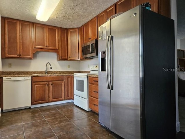 kitchen featuring brown cabinetry, dark tile patterned flooring, a sink, appliances with stainless steel finishes, and a textured ceiling