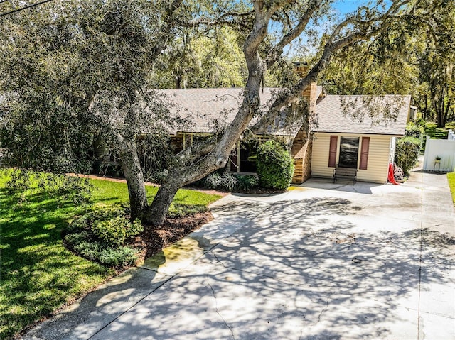 view of front of home with entry steps, a front lawn, concrete driveway, and roof with shingles