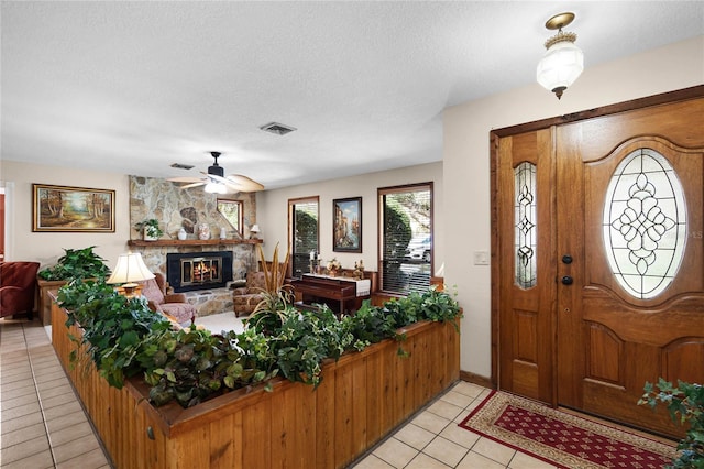 entrance foyer featuring light tile patterned floors, visible vents, a ceiling fan, a textured ceiling, and a stone fireplace