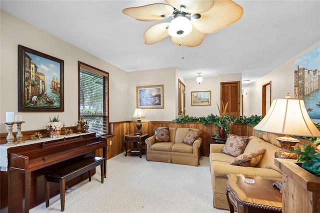 living area featuring a wainscoted wall, wooden walls, a ceiling fan, and light colored carpet