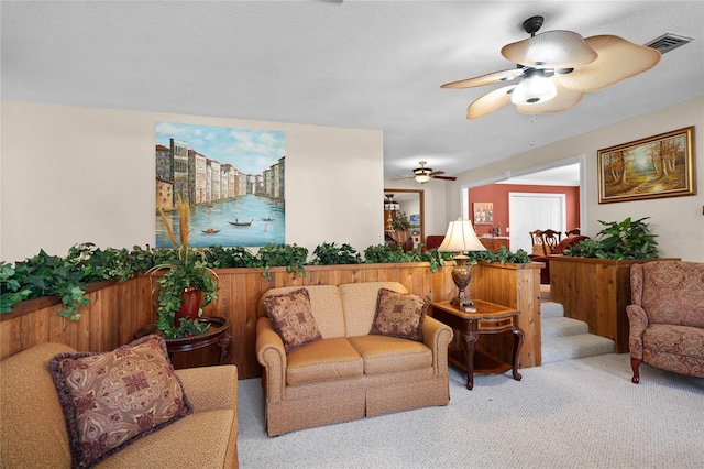 carpeted living room with stairway, visible vents, and a ceiling fan