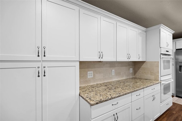 kitchen featuring light stone counters, white cabinets, dark wood finished floors, and white double oven