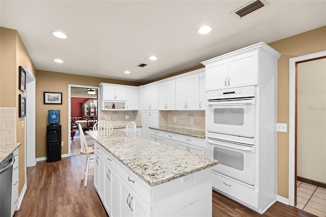 kitchen with white cabinets, visible vents, a kitchen island, and white double oven