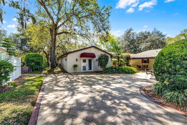 view of front of home featuring concrete driveway, french doors, and fence