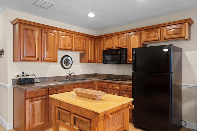 kitchen featuring visible vents, brown cabinetry, a textured ceiling, black appliances, and a sink