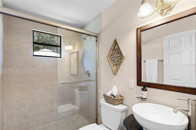 full bathroom with a textured wall, a sink, a shower stall, and toilet