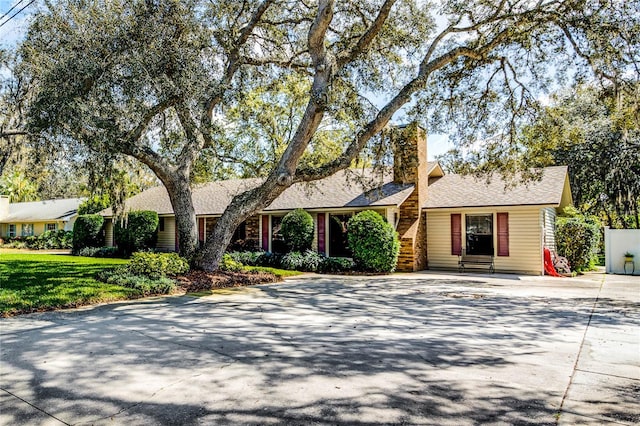 ranch-style house featuring a chimney, concrete driveway, and a front yard