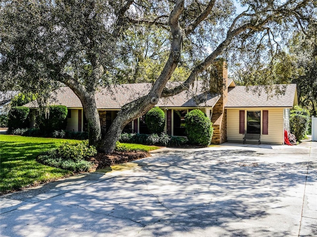 view of front of house with entry steps, concrete driveway, a chimney, and a front lawn