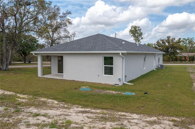 view of property exterior with stucco siding, roof with shingles, a yard, and central AC unit