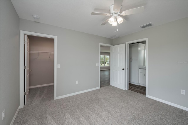 unfurnished bedroom with carpet, a walk in closet, visible vents, and baseboards