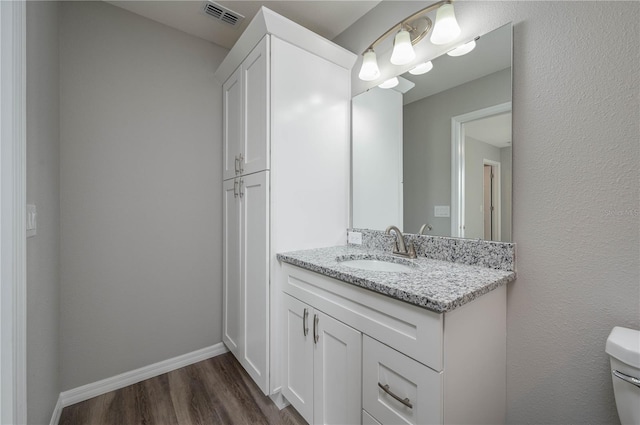 bathroom featuring baseboards, visible vents, toilet, wood finished floors, and vanity