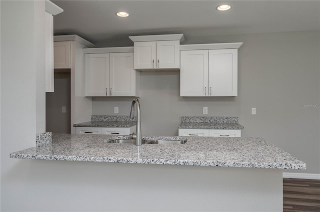 kitchen with dark wood-style floors, recessed lighting, white cabinets, a sink, and light stone countertops