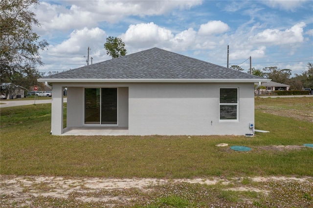 rear view of house with a shingled roof, a yard, and stucco siding