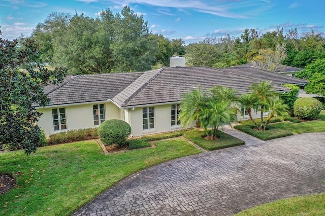 ranch-style home with a tile roof, decorative driveway, stucco siding, a front lawn, and a chimney