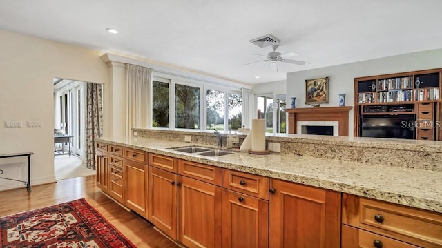 kitchen featuring light stone counters, a sink, visible vents, light wood finished floors, and brown cabinetry