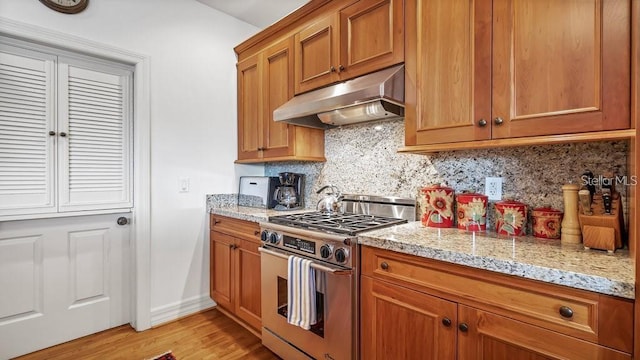 kitchen featuring under cabinet range hood, high end range, brown cabinets, light wood finished floors, and tasteful backsplash