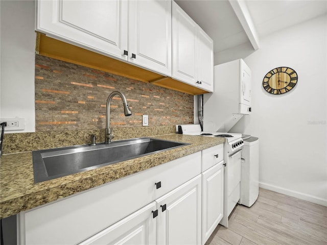 kitchen with white electric range oven, tasteful backsplash, white cabinetry, a sink, and baseboards