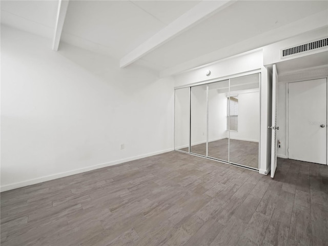 unfurnished bedroom featuring baseboards, visible vents, beamed ceiling, wood finished floors, and a closet