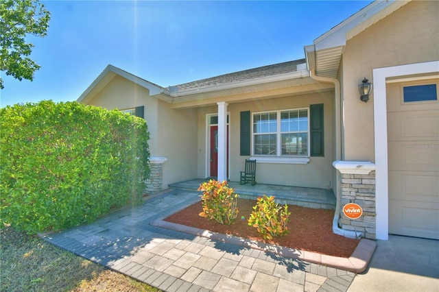 doorway to property with stucco siding, roof with shingles, a porch, and an attached garage