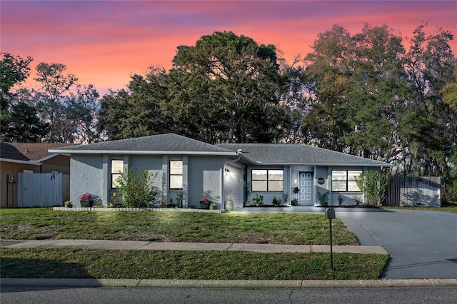 ranch-style house with a yard, fence, and stucco siding