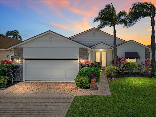 ranch-style house featuring a front yard, an attached garage, stucco siding, stone siding, and decorative driveway