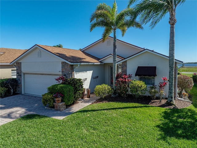 ranch-style home with stucco siding, decorative driveway, stone siding, a front yard, and a garage