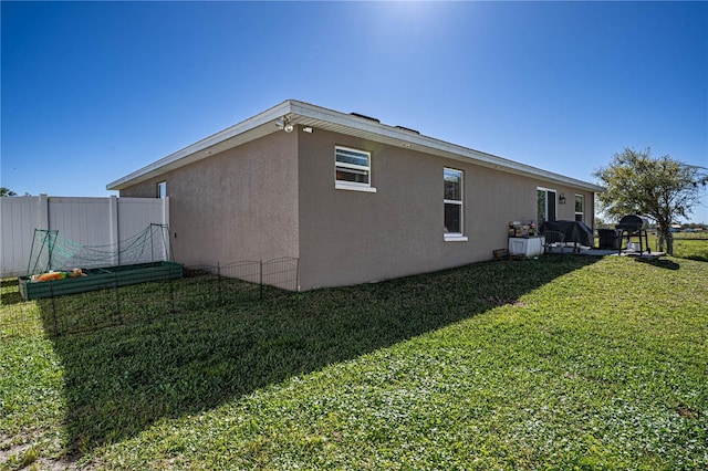 view of side of property with fence, a lawn, and stucco siding