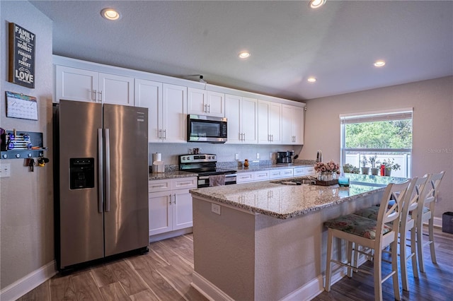 kitchen featuring appliances with stainless steel finishes, a kitchen island with sink, white cabinetry, a sink, and wood finished floors