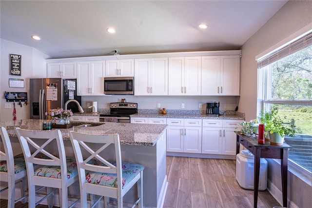 kitchen featuring light stone counters, stainless steel appliances, a sink, white cabinetry, and light wood-type flooring