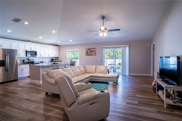 living room featuring a wealth of natural light, dark wood-type flooring, visible vents, and a ceiling fan