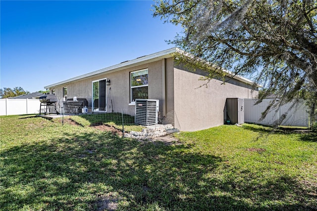 back of house with central air condition unit, a fenced backyard, a yard, and stucco siding