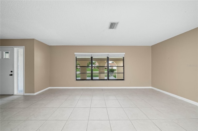 empty room with light tile patterned floors, a textured ceiling, visible vents, and baseboards