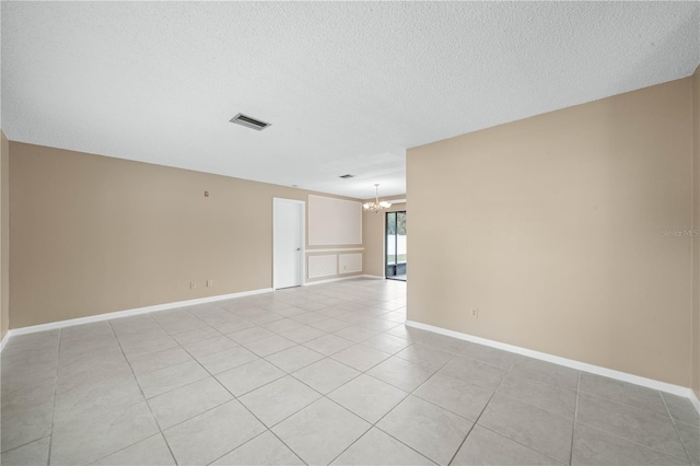 unfurnished room featuring a textured ceiling, baseboards, visible vents, and a notable chandelier