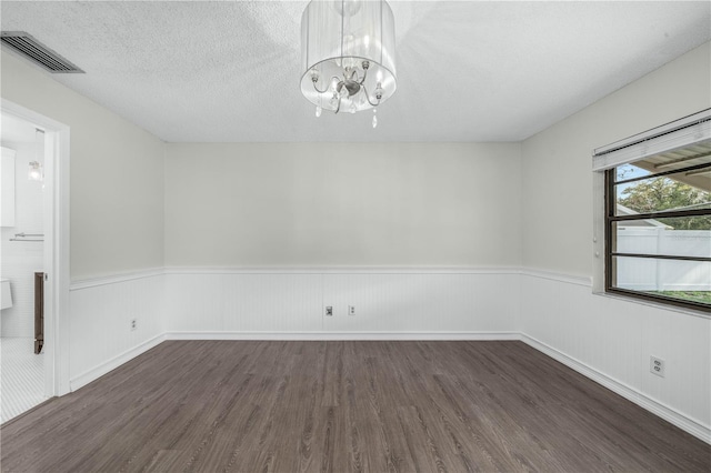 unfurnished room featuring dark wood-type flooring, wainscoting, visible vents, and a textured ceiling