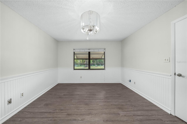 spare room with a chandelier, dark wood-style flooring, wainscoting, and a textured ceiling