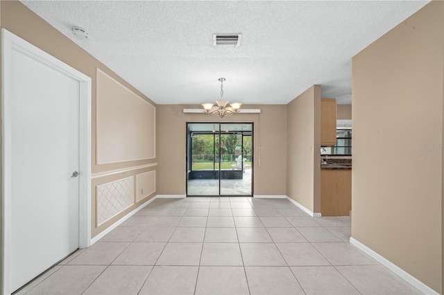 empty room featuring light tile patterned floors, visible vents, baseboards, a textured ceiling, and a chandelier