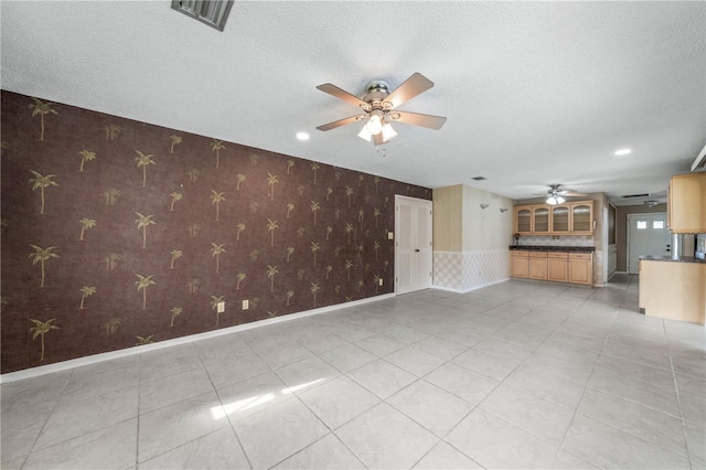 unfurnished living room with a textured ceiling, light tile patterned floors, a ceiling fan, baseboards, and wallpapered walls