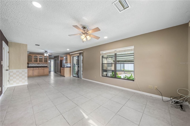 unfurnished living room featuring light tile patterned floors, a textured ceiling, visible vents, baseboards, and a ceiling fan