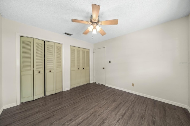 unfurnished bedroom with dark wood-style flooring, multiple closets, visible vents, a textured ceiling, and baseboards