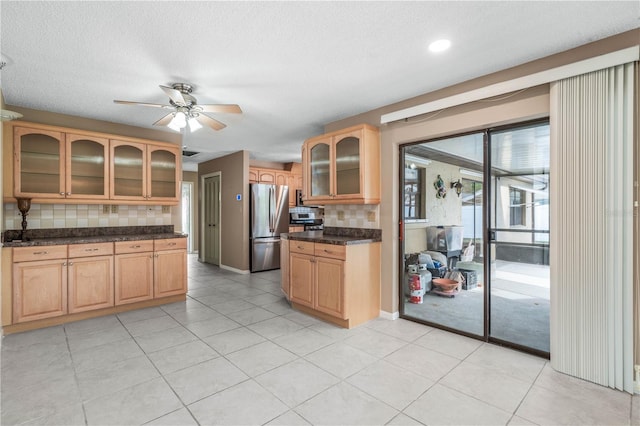 kitchen with backsplash, glass insert cabinets, freestanding refrigerator, a ceiling fan, and light brown cabinets