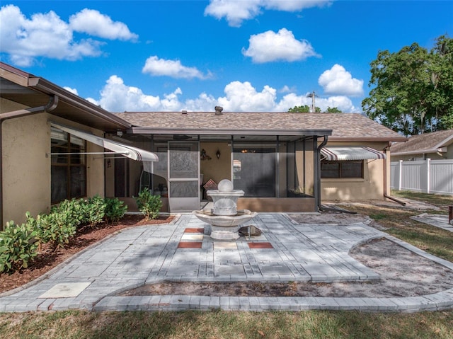 back of property with stucco siding, a shingled roof, a sunroom, a patio area, and fence