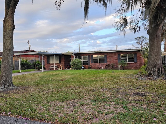 single story home featuring driveway, a front lawn, an attached carport, and brick siding