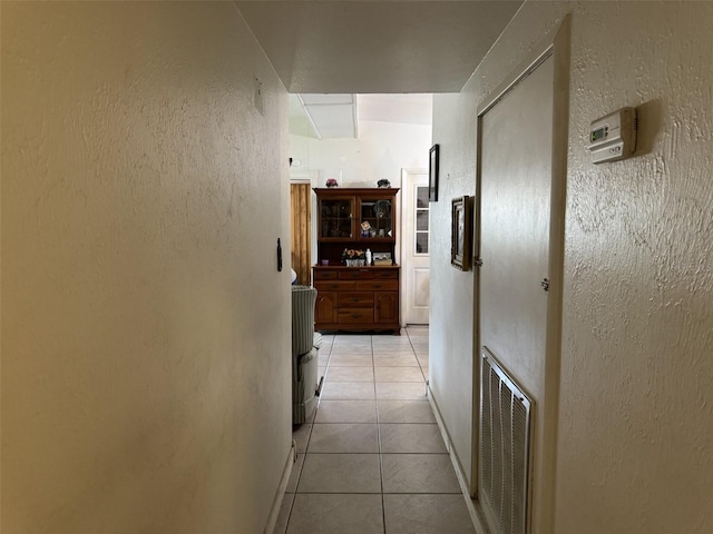 hall featuring visible vents, a textured wall, and light tile patterned floors