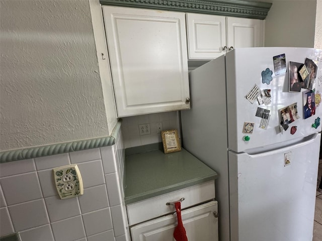 kitchen featuring a textured wall, dark countertops, freestanding refrigerator, and white cabinetry