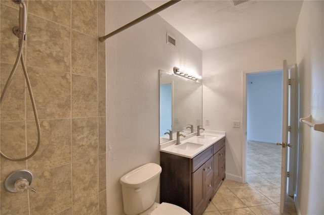 bathroom featuring double vanity, visible vents, tiled shower, toilet, and a sink