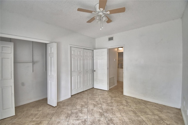 unfurnished bedroom with a textured ceiling, light tile patterned flooring, visible vents, baseboards, and multiple closets