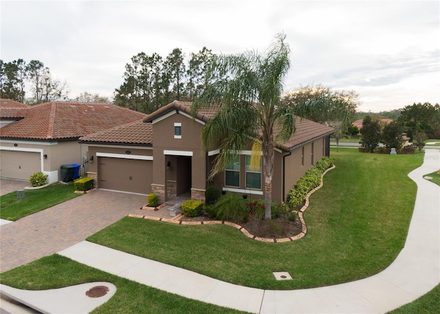 view of front of home with a front yard, an attached garage, stucco siding, a tile roof, and decorative driveway