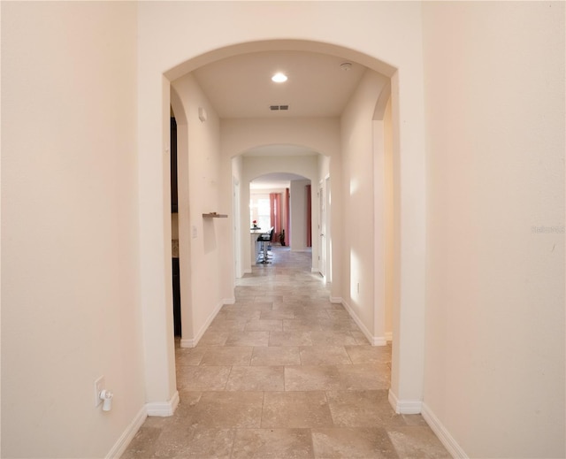 hallway featuring visible vents, arched walkways, baseboards, and stone finish flooring